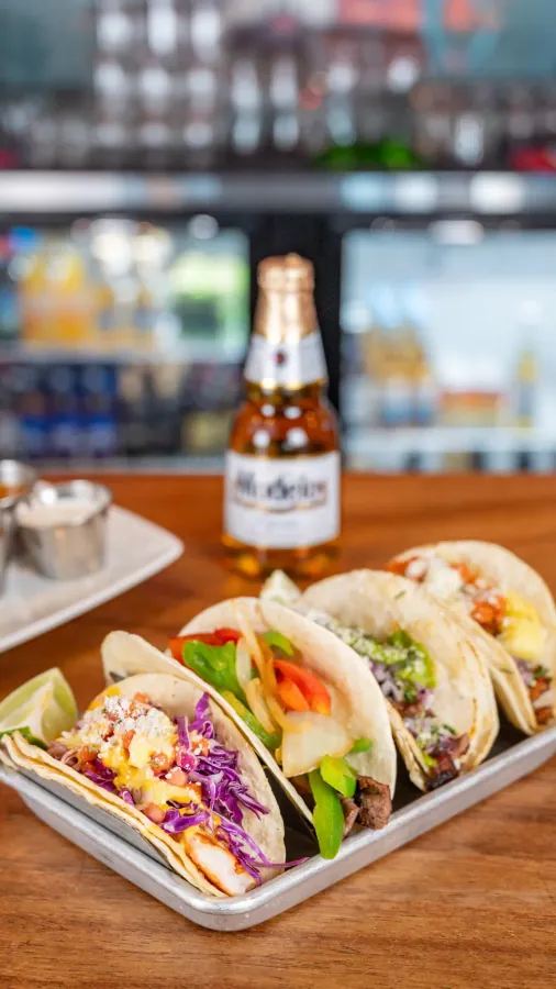 Three street tacos with a bottle of Mexican beer
